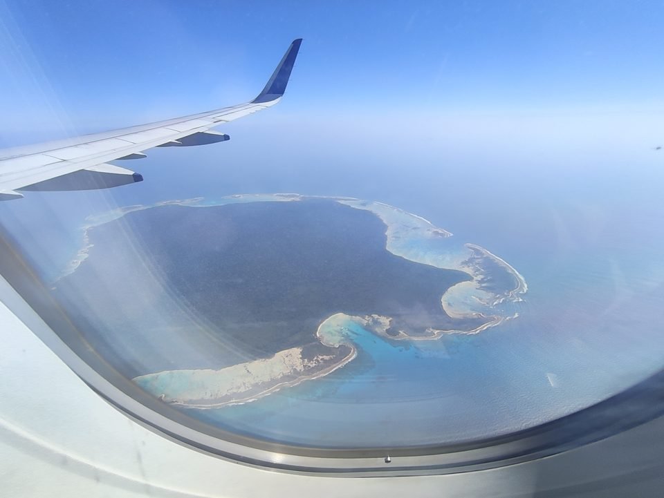 A ilha Sentinela do Norte vista pela janela de um avião comercial, com a asa no alto e o recife turquesa em volta da floresta