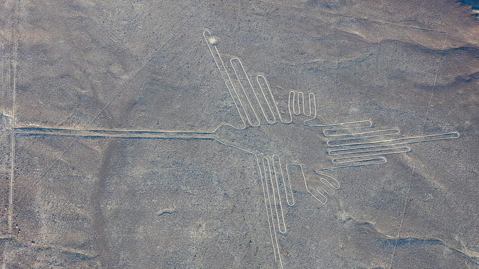 Vista aérea do geoglifo do beija-flor de Nazca, desenhado em linha clara contínua sobre o deserto cinza, com bico longo e asas abertas