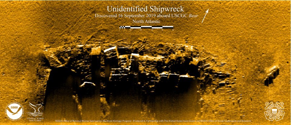 Imagem de sonar lateral em tons de âmbar mostrando um naufrágio no fundo do mar: o casco aparece como um relevo claro e irregular, com longas sombras escuras projetadas para baixo