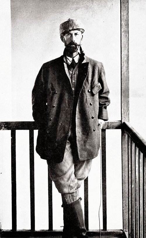 Fotografia de Percy Fawcett em 1911, de pé numa varanda, com roupa de campo e chapéu