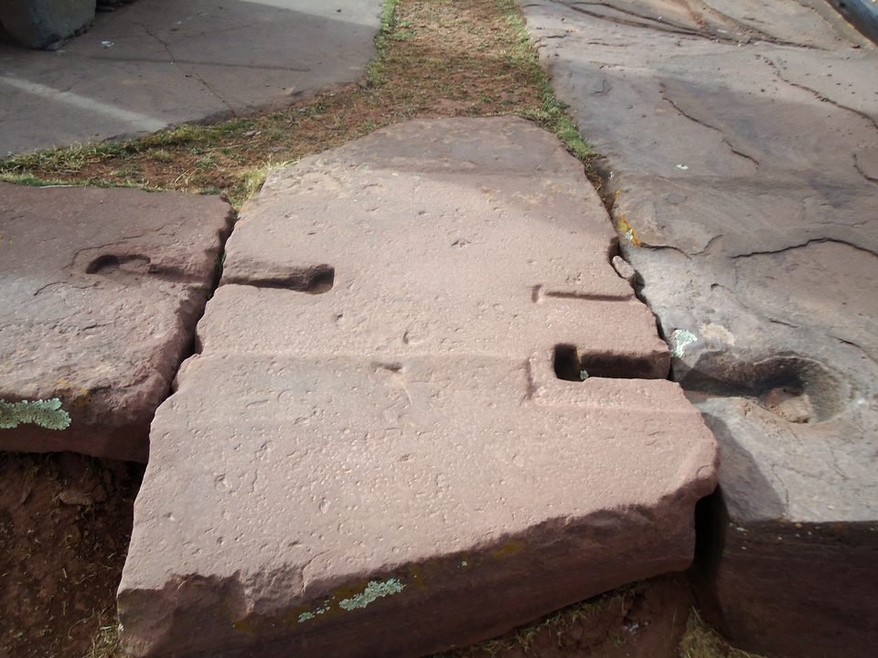 Reddish sandstone slabs joined at a seam; on either side of the seam there are shallow T- and I-shaped sockets, empty, where metal cramps once fitted