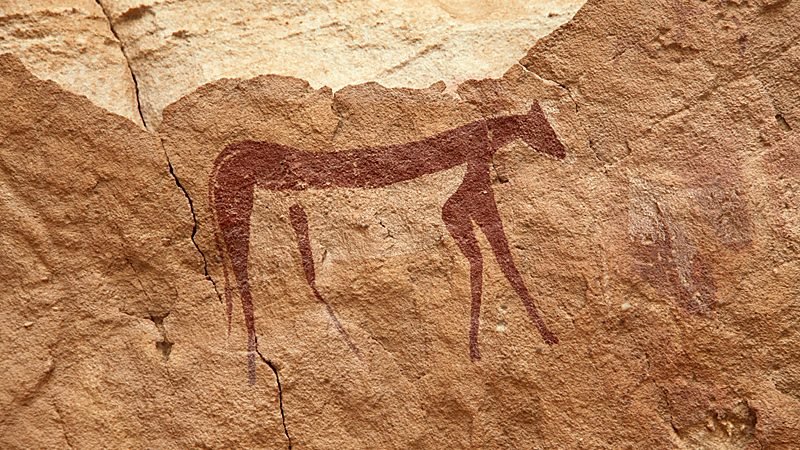 Pintura rupestre de um quadrúpede de pernas longas em ocre avermelhado sobre arenito claro