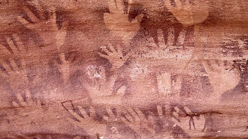 Dezenas de mãos humanas em negativo pintadas em ocre sobre a parede do abrigo Foggini-Mesticawi