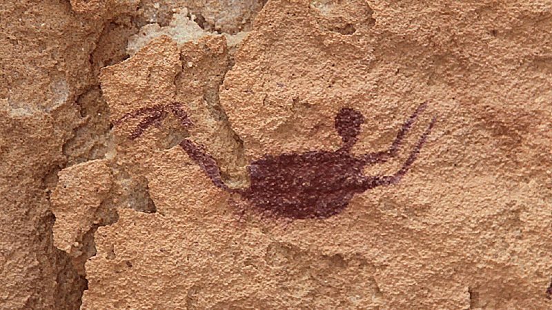 Pintura rupestre de uma figura humana na horizontal, de braços e pernas abertos, sobre arenito claro na caverna dos nadadores